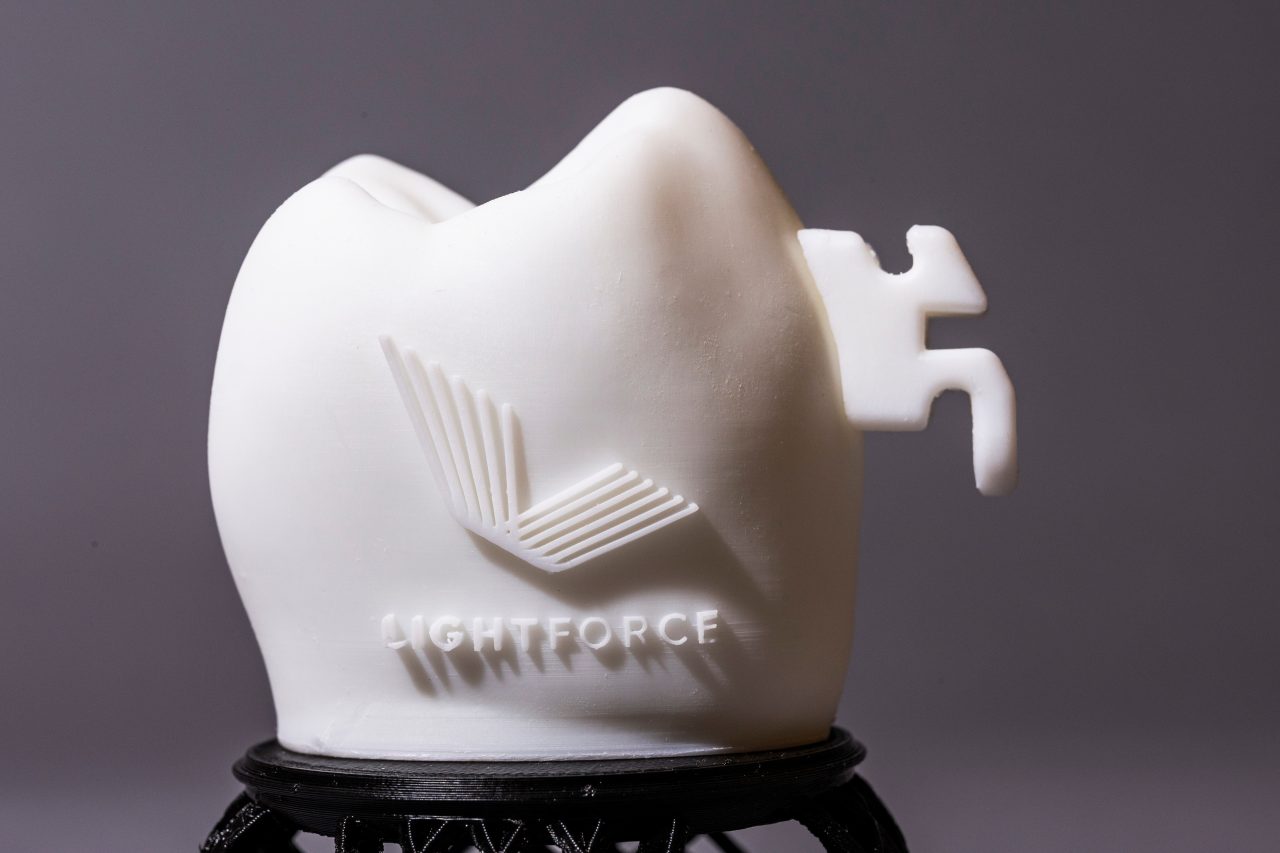 3D Printed ceramic model of a tooth with a lightforce logo embossed on it. The model has a mounted white colored LightForce braces bracket.